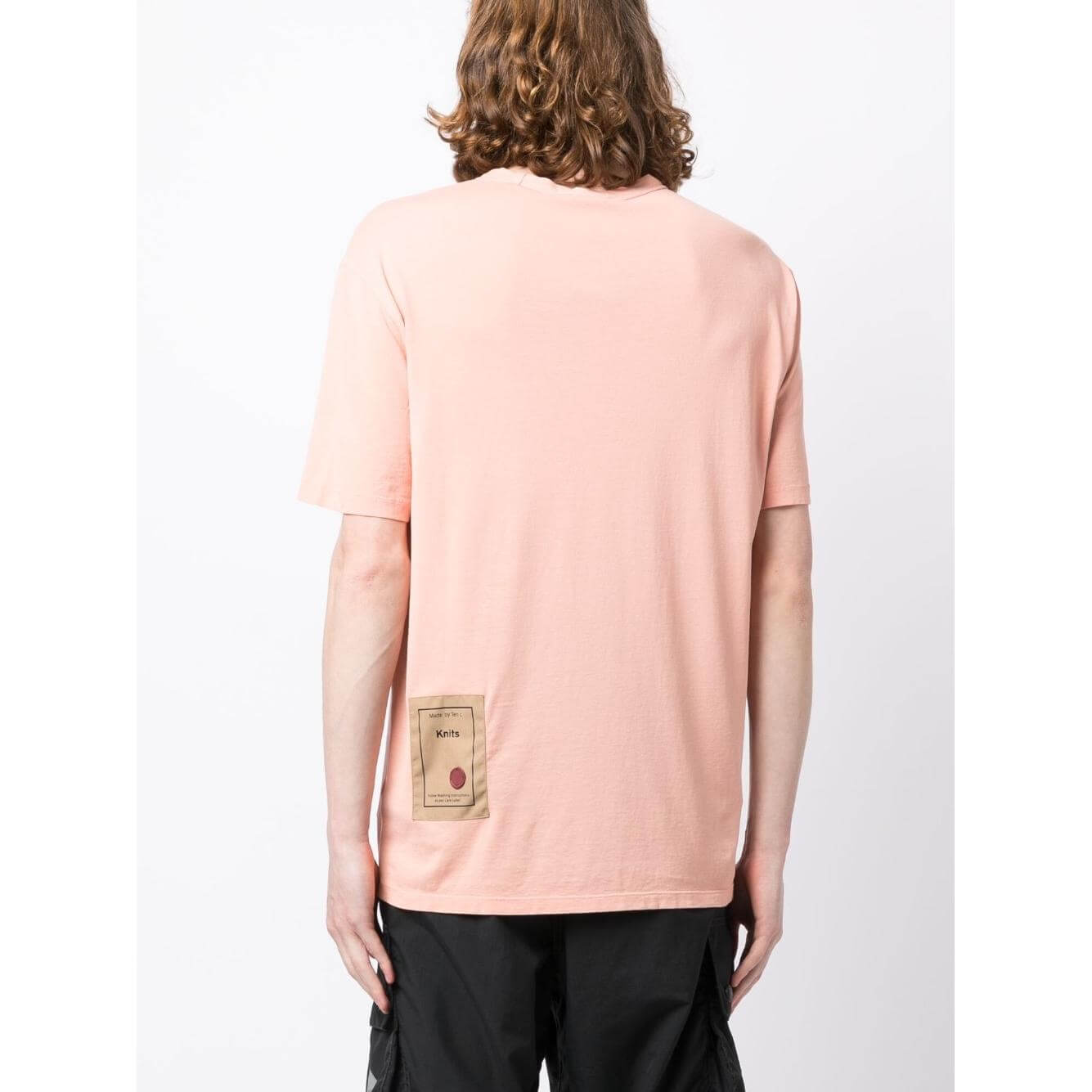 Back view of a TEN C coral pink round-neck T-shirt with logo patch on the rear, worn by a model. Cotton material and short sleeves.