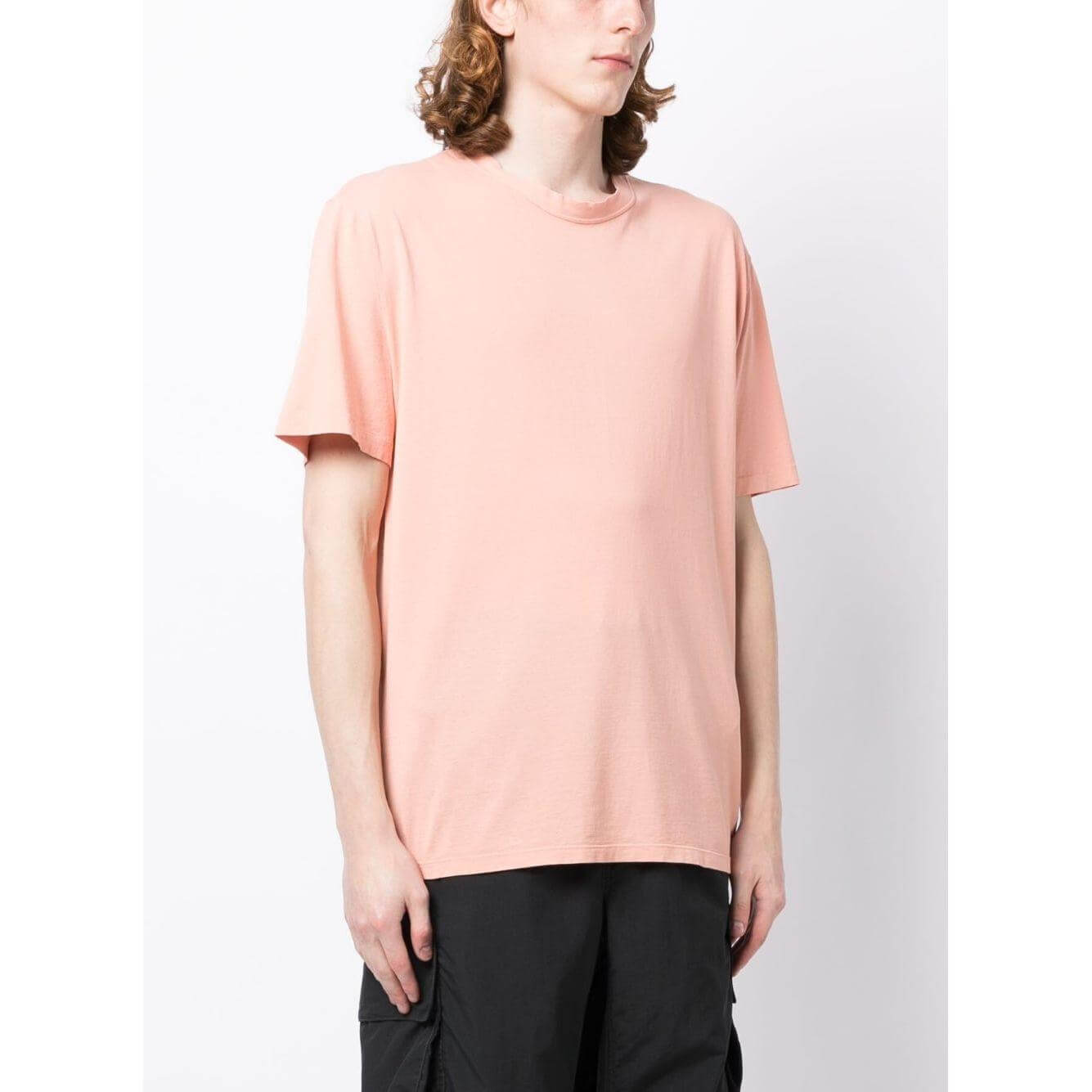 Person wearing a coral pink TEN C round-neck T-shirt with short sleeves and a logo patch. Fashionable casual wear.
