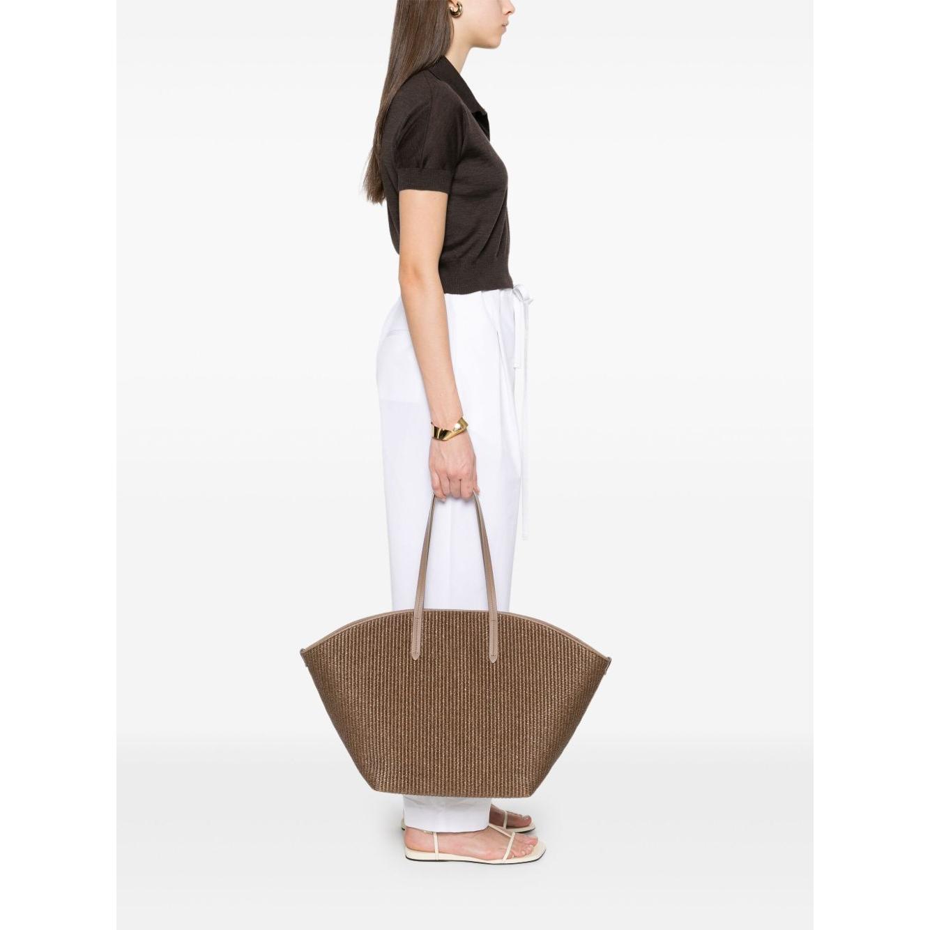 Side view of woman holding a Brunello Cucinelli brown woven tote bag with signature Monili chain and flat top handles.