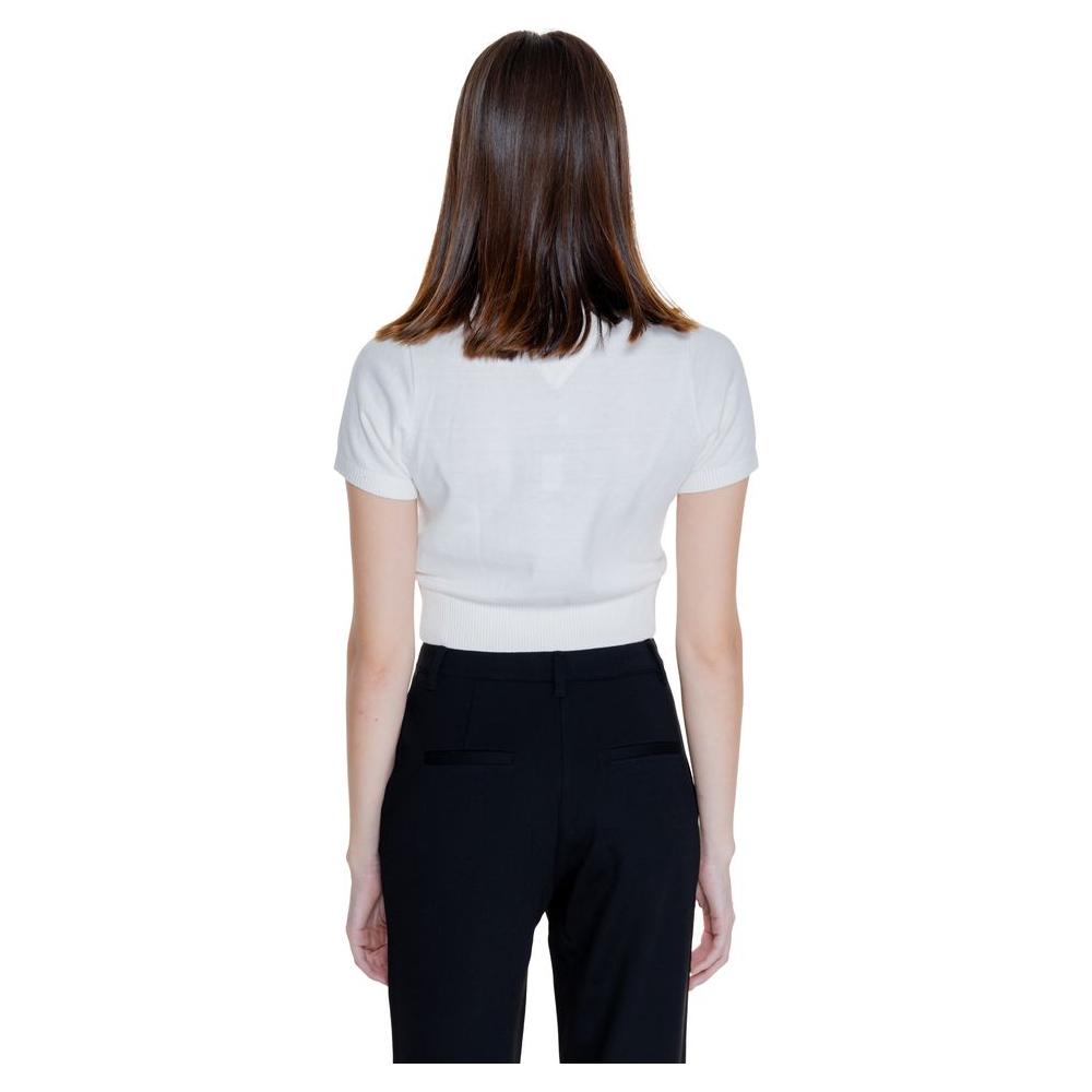 Back view of a woman wearing a white Tommy Hilfiger short sleeve top, yarn knit, from the Fall/Winter collection, paired with black pants.