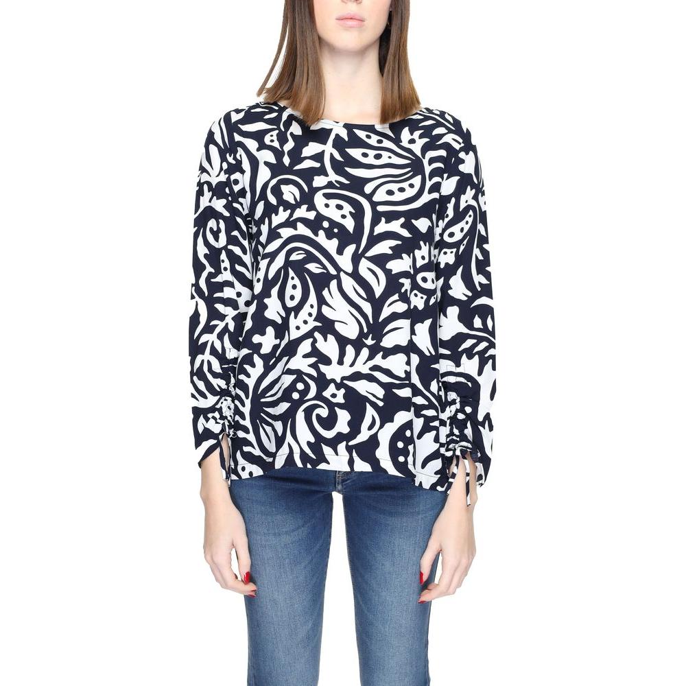 Woman wearing a black and white patterned long sleeve blouse paired with blue jeans.